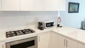 Une cuisine avec des meubles blancs, une cuisinière à gaz, un four à micro-ondes et une petite plante en pot.