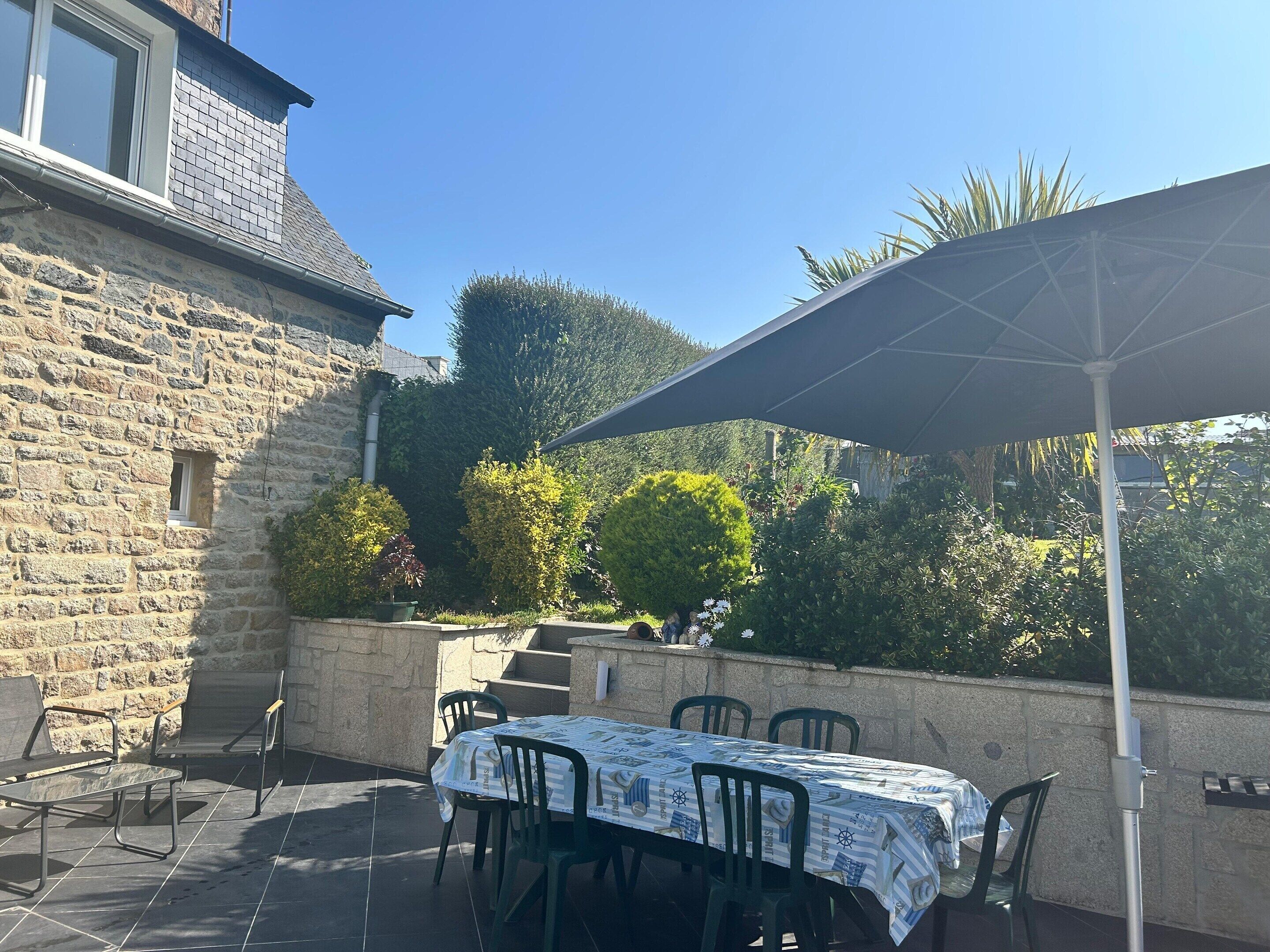 An outdoor patio with a table and chairs, a stone wall, and a large umbrella.