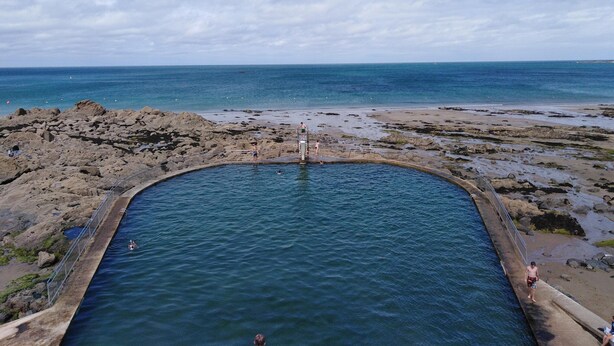 Una playa rocosa con una piscina y un muelle que se adentra en el agua.