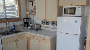 A compact kitchen with wooden cabinets, a refrigerator, a microwave, a toaster, and a coffee maker.