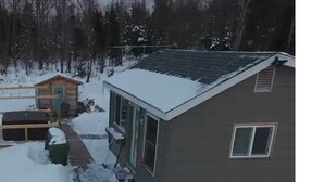 A house with a sloped roof and a small window. Snow covers the ground and the roof.