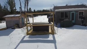 A wooden deck with a table and chairs, a small shed, and a house with a door and window.