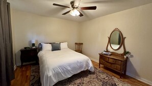 A bedroom with a bed, a dresser, a mirror, a ceiling fan, and a nightstand with a lamp. - Main Street Condo in Miles City (Miles City)