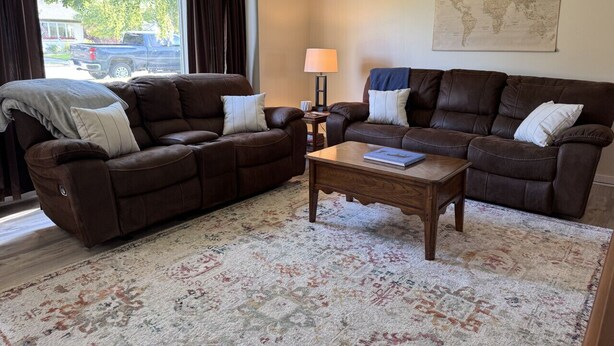 A living room with two brown leather sofas, a wooden coffee table, and a patterned rug. - Main Street Condo in Miles City (Miles City)