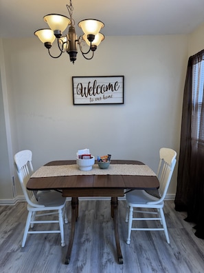 Ein Esszimmer mit Holztisch, weißen Stühlen, einer Chandelierleuchtre und einem Willkommen-Schild an der Wand.