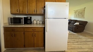 A compact kitchen with wooden cabinets, a white refrigerator, a microwave, and a coffee maker. - Main Street Condo in Miles City (Miles City)