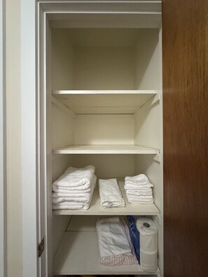 Ein Schrank mit drei Regalen; das untere Regal enthält gefaltete Handtücher und eine Packung Toilettenpapier.