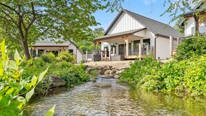 A house with a covered porch, a small stream, and lush greenery.