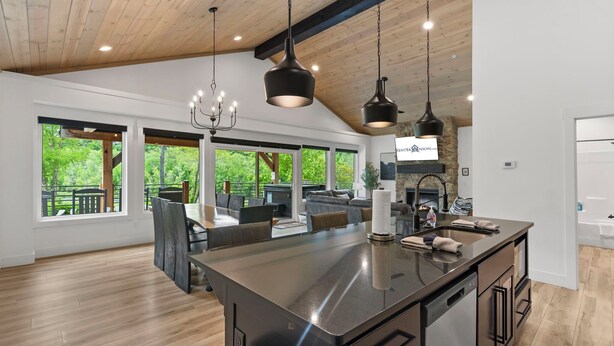 A spacious kitchen with a large island, modern pendant lighting, and a view of the outdoors through large windows.