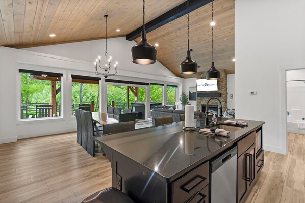 A spacious kitchen with a large island, modern pendant lighting, and a view of a lush outdoor area.