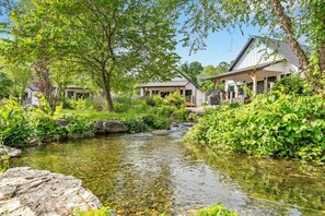 A riverside property with a wooden bridge, lush greenery, and a clear stream.