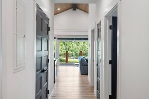 A hallway with a wooden floor leading to a covered outdoor area with a blue sofa.