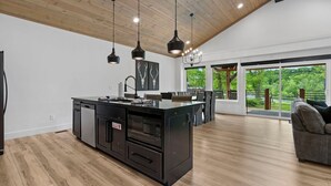 A modern kitchen with a central island, wooden flooring, and pendant lighting.