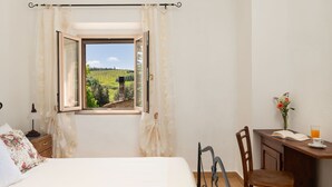 A bedroom with a large window, a bed, a desk with a chair, and a small table with a vase and a glass of orange juice. - Annalisa by Interhome (Montaione)
