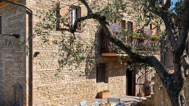 A stone building with a table set for a meal outside, surrounded by olive trees and potted plants. - Annalisa by Interhome (Montaione)