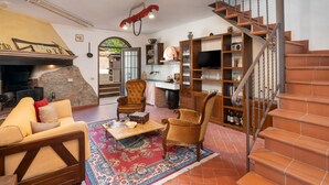 A cozy living room with a fireplace, a wooden staircase, and a kitchen area. - Annalisa by Interhome (Montaione)