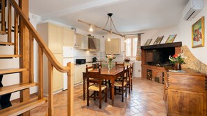 A kitchen with a wooden staircase, a dining table with chairs, a fireplace, and a hanging light fixture. - Annalisa by Interhome (Montaione)