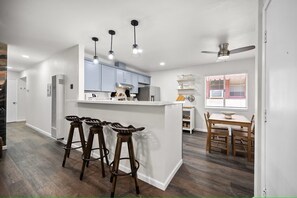 Een moderne keuken met een centraal eiland, barkrukken en een eethoek met een tafel en stoelen.