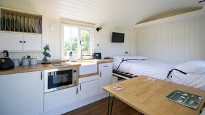 A compact room with a kitchenette, a bed, a TV, and a window.