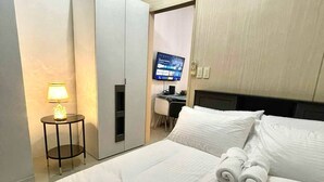 A hotel room with a bed, a desk with a computer, and a TV on the wall. - Jazz Residences Tower B +Wifi & Netflix (Makati)