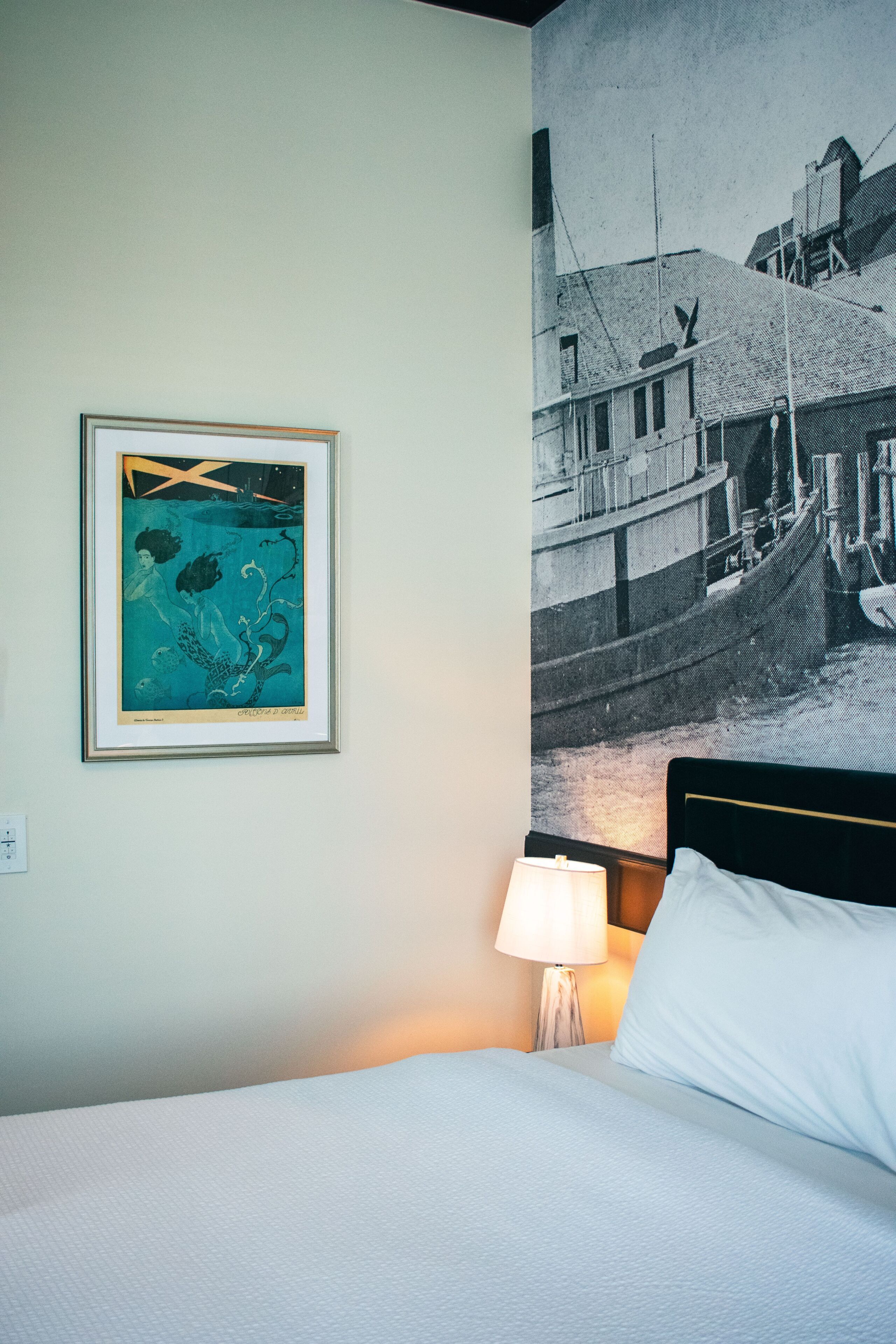 Quarto de hotel com uma cama, um quadro na parede e uma fotografia grande em preto e branco.