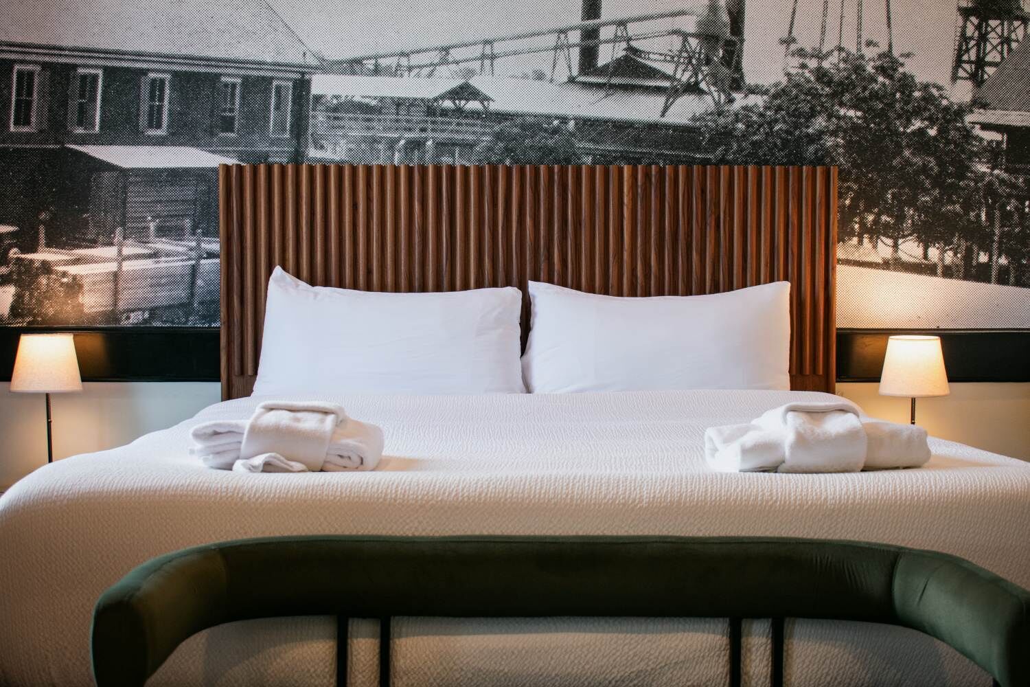 A hotel room with a bed, two pillows, two lamps, and a view of a building through a window.