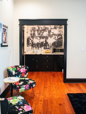 A room with a wooden floor, a black cabinet with drawers, a floral chair, a small round table, and a wall-mounted picture. - The Montgomery by Visit Apalach (Apalachicola)