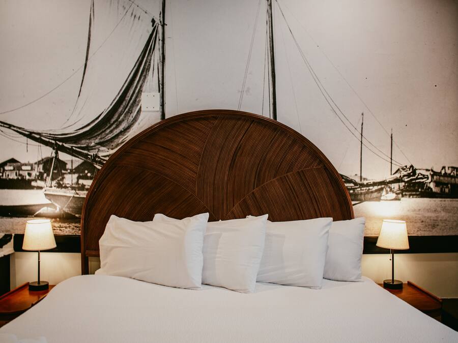 A hotel room with a large bed, two bedside tables with lamps, a wooden headboard, and a large wall mural.