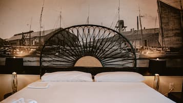 Una cama con cabecera, sábanas blancas y una lámpara fijada a la pared.