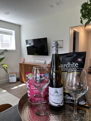 A dining table with a bottle of wine, a glass, a packet of snacks, and a box of chocolate.