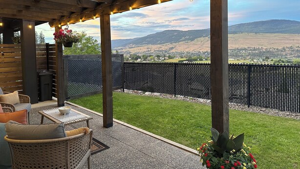 A covered patio with outdoor furniture, a pergola with string lights, and a view of a town and hills in the background.