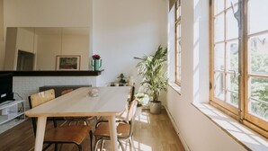 A spacious dining area with a large wooden table and chairs, a brick wall, and a window with a view of greenery. - 1 bedroom apartment in Liege center, Place du Marché - 3rd floor (Liège)