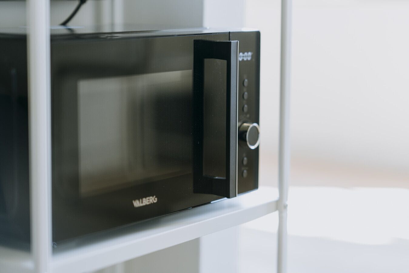 Een zwarte magnetron met een digitaal display en bedieningspaneel, gemonteerd op een witte kast.
