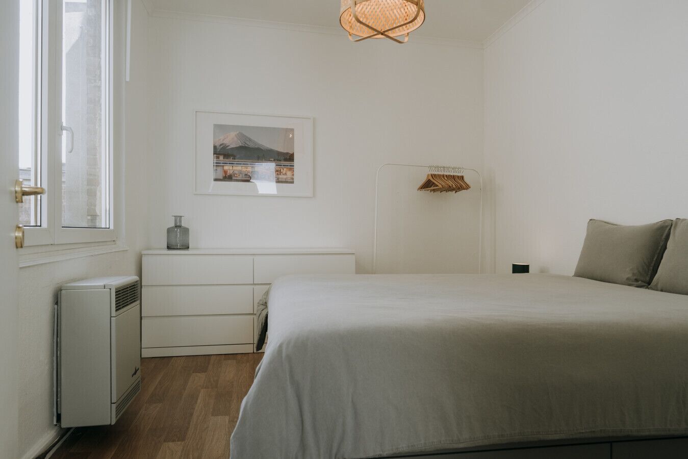 Een slaapkamer met een bed, een kaptafel, een radiator, een lijst met een afbeelding en een hanglamp.