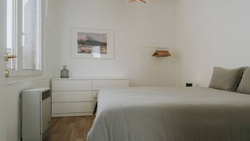Een slaapkamer met een bed, een kaptafel, een radiator, een lijst met een afbeelding en een hanglamp.