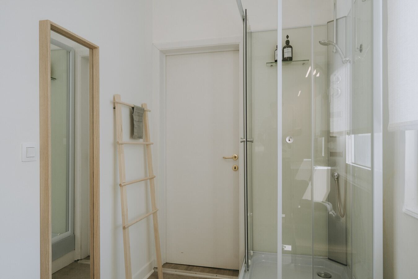 Une salle de bain avec une douche à parois de verre, une échelle en bois et une porte blanche.