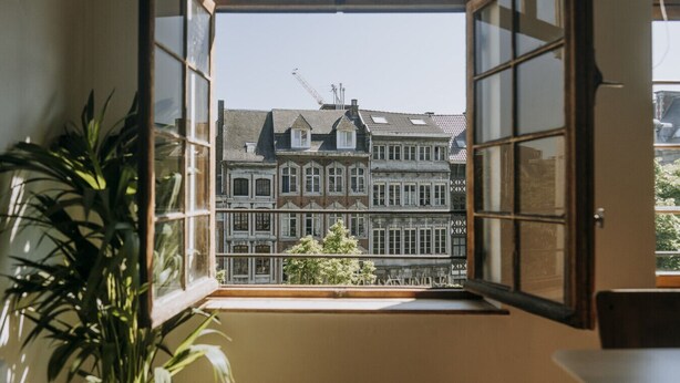 An open window with a view of a multi-story building with a crane on the roof, a balcony, and a potted plant inside. - 1 bedroom apartment in Liege center, Place du Marché - 3rd floor (Liège)