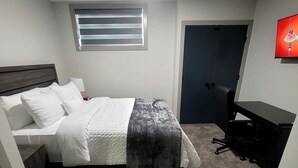Une chambre à coucher comprenant un lit, un bureau, une chaise, un téléviseur et une fenêtre avec des stores.