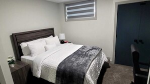Een slaapkamer met een bed, nachtkastje, lamp, raam en een deur.