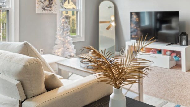 Una sala de estar con sofá, televisor, un árbol de Navidad y una planta decorativa.