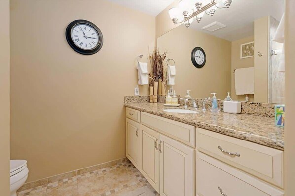 A bathroom with a sink, mirror, two clocks, and a toilet. - Maui Retreat with Refreshing Pool and Walk 2 Beach (Lahaina)