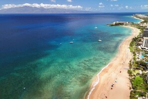An aerial view of a coastal resort with a beach, clear blue waters, and a mountain in the background. - Maui Retreat with Refreshing Pool and Walk 2 Beach (Lahaina)