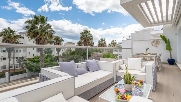A rooftop terrace with white sofas, a dining table, and a potted plant.