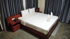 A neatly made bed with white linens, a wooden headboard, and a bedside table with a phone. - LISEKA HOTEL (Phnom Penh)
