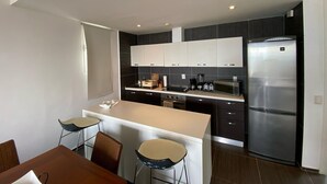 A modern kitchen with a central island, dark cabinetry, and stainless steel appliances. - Apartamento Vista Mare 16-301 (Samaná)