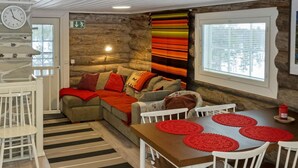 A cozy room with a sofa, a dining table with red placemats, a clock, and a window with blinds.