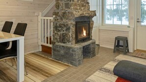 A cozy interior with a stone fireplace, a dining area with chairs, a staircase, and a window with a view.