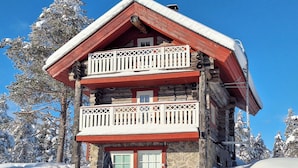 A log cabin with a balcony, stone foundation, and a snow-covered roof.