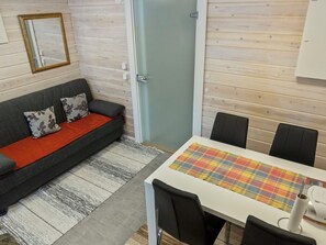 A room with a sofa, a dining table with chairs, a door, and a mirror on the wall.