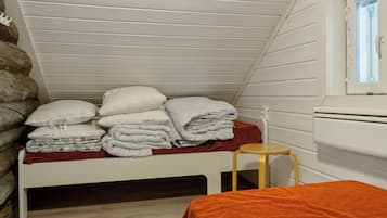 Una stanza piccola con un letto singolo, soffitto spiovente, una finestra e un termosifone.